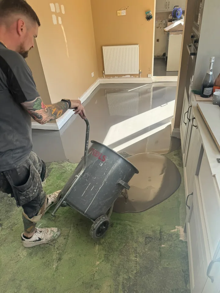 An installer pouring grey floor preparation compound around kitchen units
